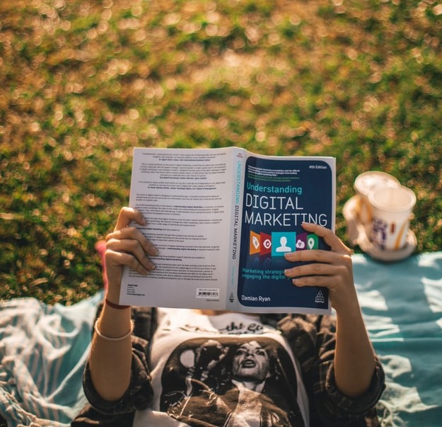 Jemand liest liegend auf einer Wiese ein Buch über digitles Marketing